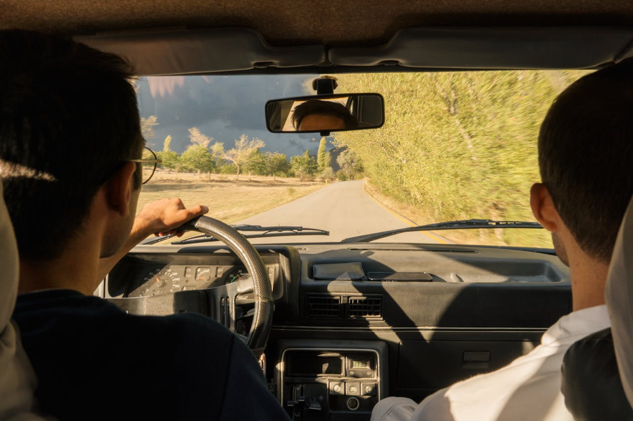 Services-03 Two adults driving through scenic countryside near Merzifon, Türkiye, in a vintage car.